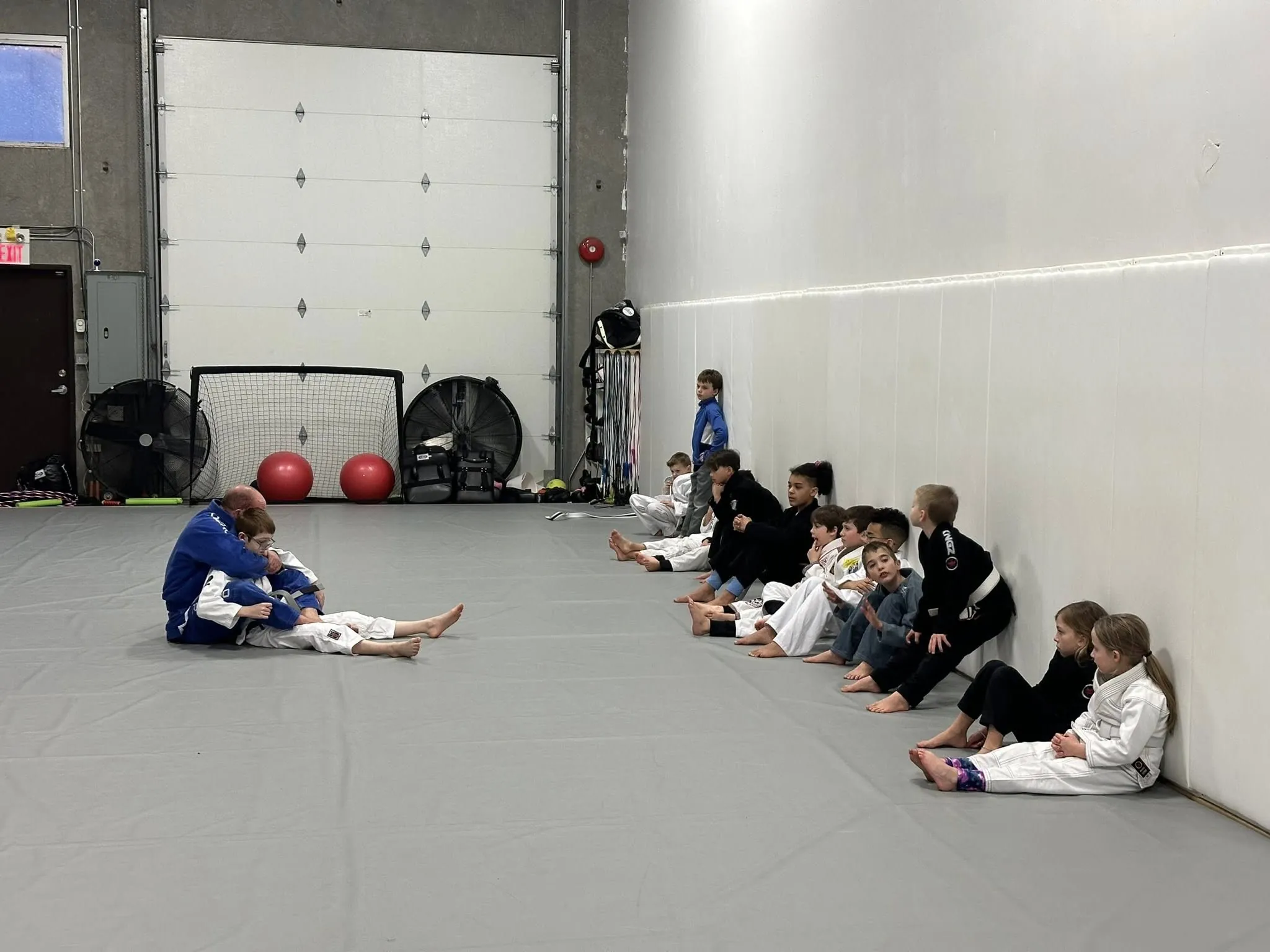 Kids in gis seated along the wall during a children's BJJ class at Mission BJJ
